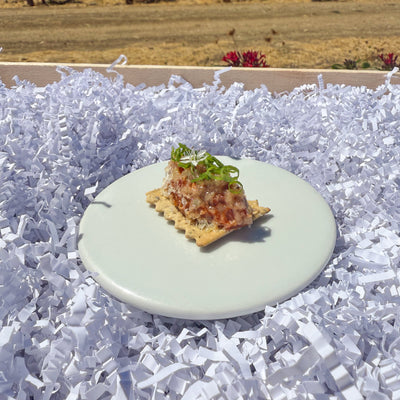 Small dish with food on a white plate over white shredded paper with vineyard background